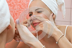 Young woman looking and squeeze acne on a face in front of the mirror. Ugly problem skin girl, teen girl having pimples