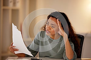Young woman looking stressed while going through paperwork alone in an office at night. One female only looking worried