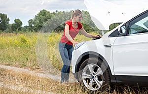 Young woman looking under the hood of broken car and trying to fix it