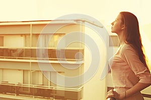 Young woman looking up on balcony apartment at sunset, blank copy space for advertising text