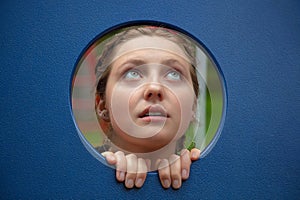 young woman looking up in kindergarten babysitter playing in game module hole blue plastic background