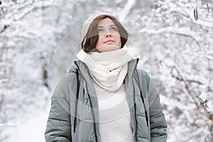 young woman looking up on winter nature, pretty beautiful girl among trees covered with snow walking in white forest and enjoying