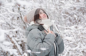 young woman looking up on winter nature, pretty beautiful girl among trees covered with snow walking in white forest and enjoying