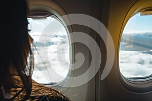 Young woman looking into window in a plane. Woman in a plane. Woman looking into porthole. Traveling by plane concept.