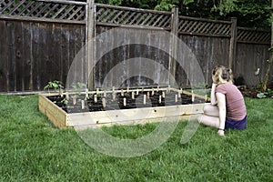 Young woman looking at a wooden raised backyard vegetable garden box