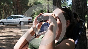 Young Woman Looks Through Binoculars While Sitting on a Chaise Longue in Nature