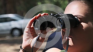 Young Woman Looks Through Binoculars While Sitting on a Chaise Longue in Nature