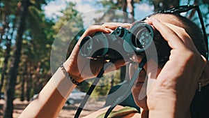 Young Woman Looks Through Binoculars While Sitting on a Chaise Longue in Nature