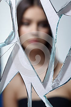 Young woman looks in a broken mirror. Out of focus portrait of beautiful female in the mirror shards