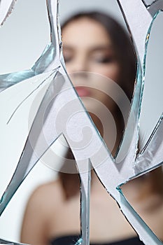 Young woman looks in a broken mirror. Out of focus portrait of beautiful female in the mirror shards