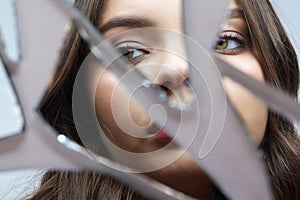 Young woman looks in a broken mirror. Portrait of beautiful female in the mirror shards