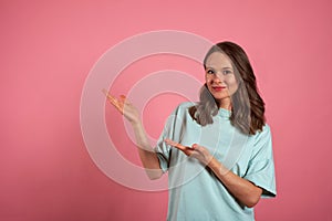 Young woman looks at the camera and pointing somewhere to the side on a pink background