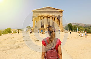 Young woman looks at Concordia Temple in the Valley of the Temples of Agrigento, Sicily. Traveler girl visits Greek Temples in