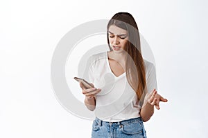 Young woman looks confused at mobile screen, reading strange message, dont understand something on phone, stare puzzled