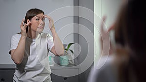 A young woman looks in the mirror. Beautiful girl is going, looking at skin.