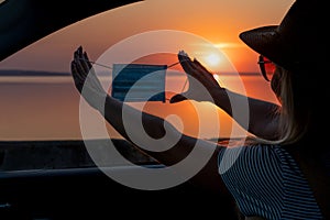 A young woman looks out the car window at the sunset on the sea.	heart made with hands