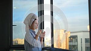 Young woman looks out window and drinks coffee in morning. Concept. Beautiful woman starts day with cup of coffee and