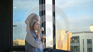 Young woman looks out window and drinks coffee in morning. Concept. Beautiful woman starts day with cup of coffee and