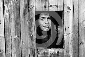 Young woman looks out of the wooden shed windows.