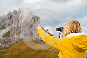 Young woman looks at Passo Giau through binoculars pointing finger