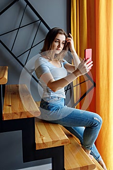 Young woman looks in smartphone and makes selfie on the staircase.