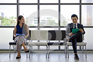 Young woman looks and smiles at a man sitting further away. Asian business people waiting for job interview by sitting spaced