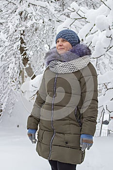A young woman looks at snow-covered trees,In winter, a woman wears warm knitted hats with a jacket and gloves