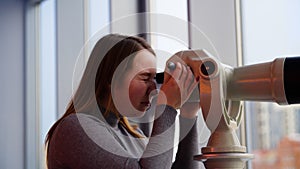 Young woman looks through stationary binoculars. Media. Beautiful woman looks through binoscope on observation deck in
