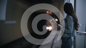 A young woman looks into the subway tunnel, the train pulls up, slow motion