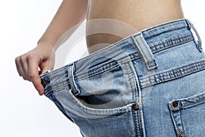 Young woman in loose jeans. Victory over excess weight and good appearance. Close-up. White background