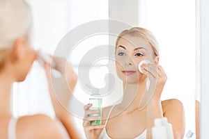 Young woman with lotion washing face at bathroom