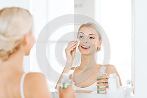 Young woman with lotion washing face at bathroom