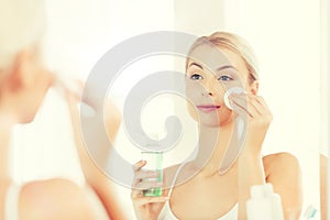 Young woman with lotion washing face at bathroom