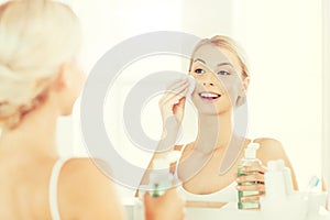 Young woman with lotion washing face at bathroom