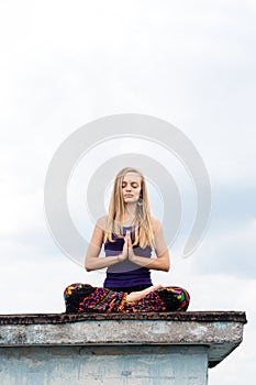 Young woman in a lotus pose on the roof