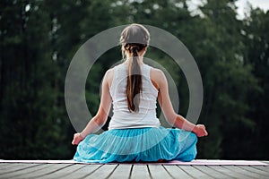 Young woman in the lotus position is practicing yoga in the forest next to the river. sitting on mats the wooden pier.