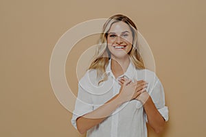 Young woman in love holding hands on chest, gazing at camera as feeling grateful and appreciative