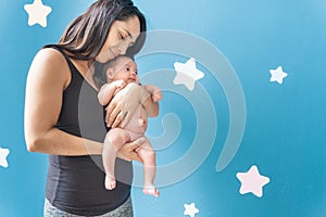 Young woman lovingly holding her baby who has an umbilical hernia on a blue background with stars