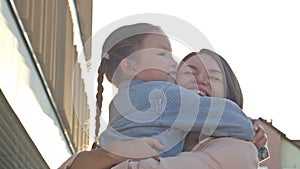 Young woman lovingly hugs a girl with pigtails 6-7 years old. Meeting or parting of mom and daughter. Mothers Day.