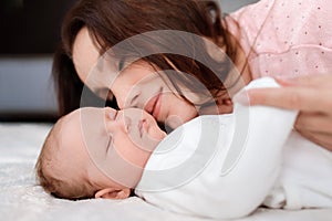 Young woman lovingly looks at her sleeping newborn daughter in the bedroom