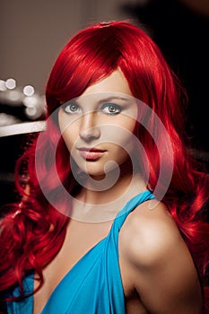 Young woman with luxurious long beautiful red hair in a blue fashionable evening dress in the rich interior.