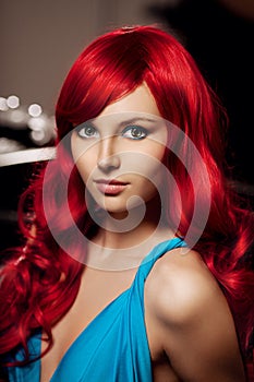 Young woman with luxurious long beautiful red hair in a blue fashionable evening dress in the rich interior.