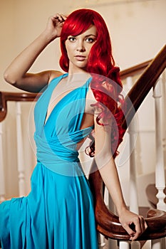 Young woman with luxurious long beautiful red hair in a blue fashionable evening dress in the rich interior.