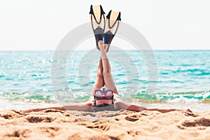 Young woman lying on the beach stretching up slender legs wearing diving mask