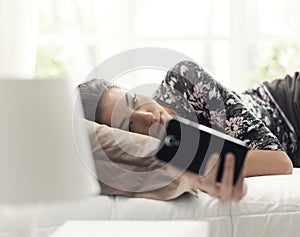 Young woman lying on the bed and connecting with her phone