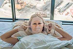 Young woman lying on a bed covered her ears because of the noise