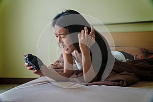 Young woman lying on a bed holding an alarm clock in her hand with exasperation