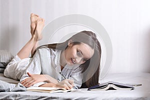 Young woman lying on the bed at home bedroom and writing into diary or planning her day, making schedule for tomorrow. Concept - r