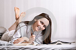 Young woman lying on the bed at home bedroom and writing into diary or planning her day, making schedule for tomorrow. Concept - r