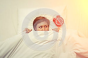 Young woman lying on the bed looking at the alarm clock in the m